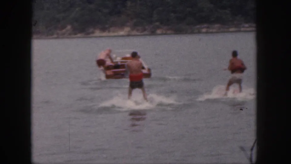 1961 Michigan lake footage frame with two men water-skiing behind a wooden motorboat.