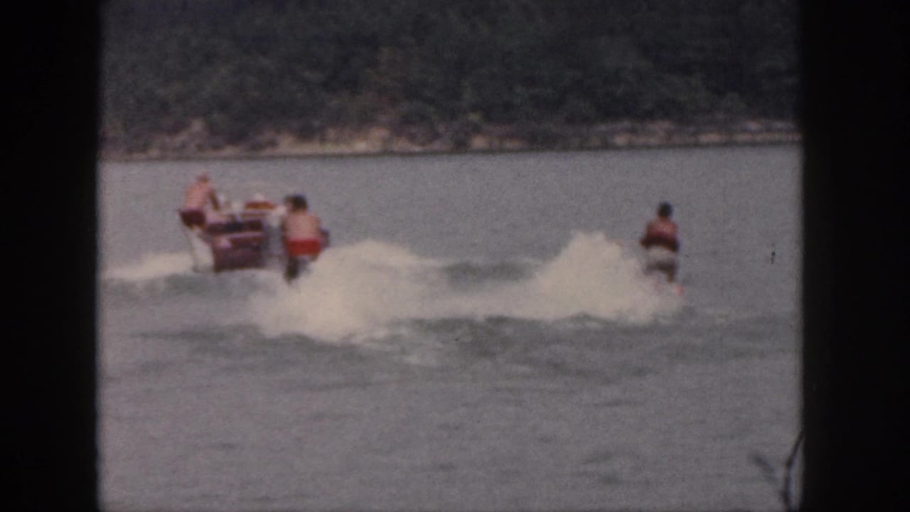 1961 Michigan lake scene with tandem water skiers trailing a small motorboat and visible wake spray.