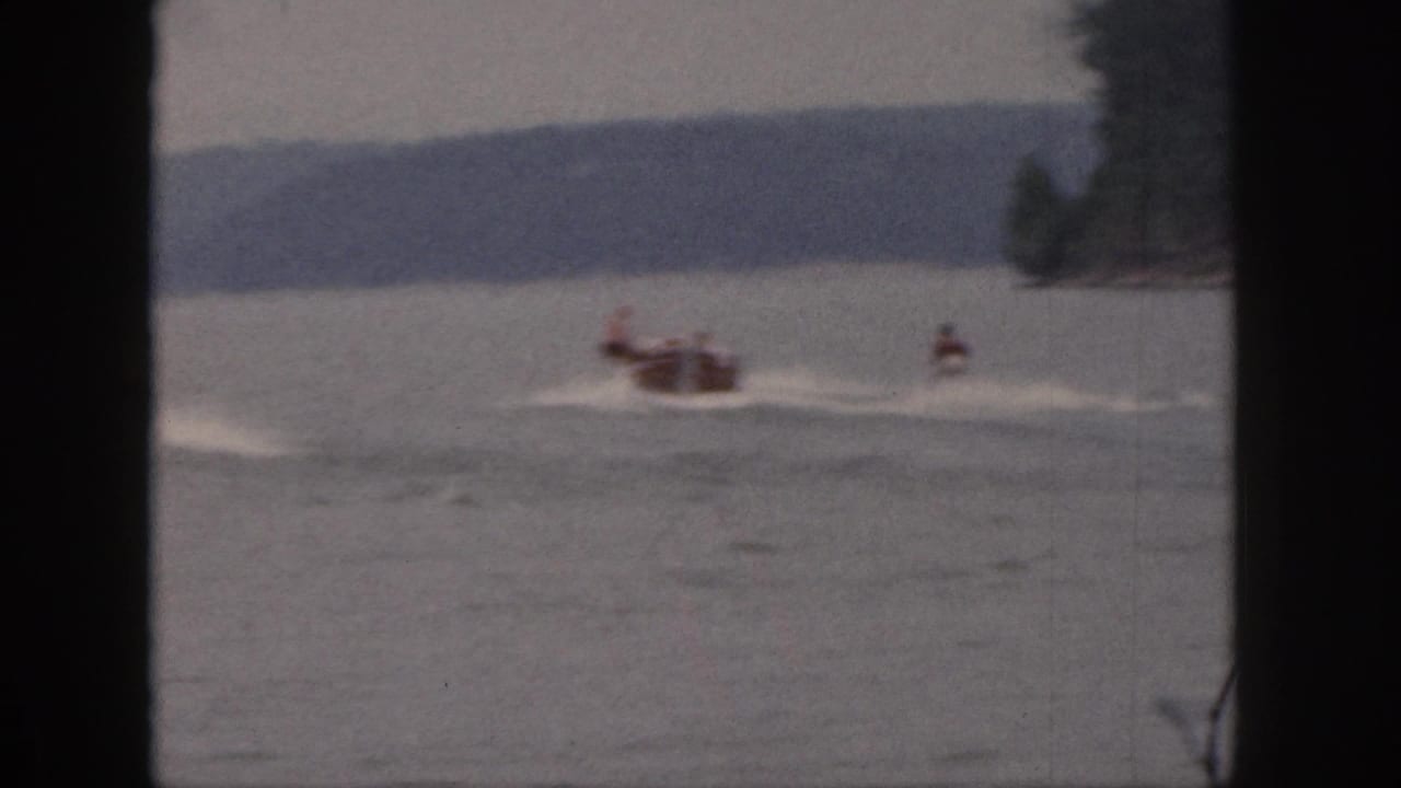 Motorboat pulls a waterskier across open water with a wooded shoreline beyond.