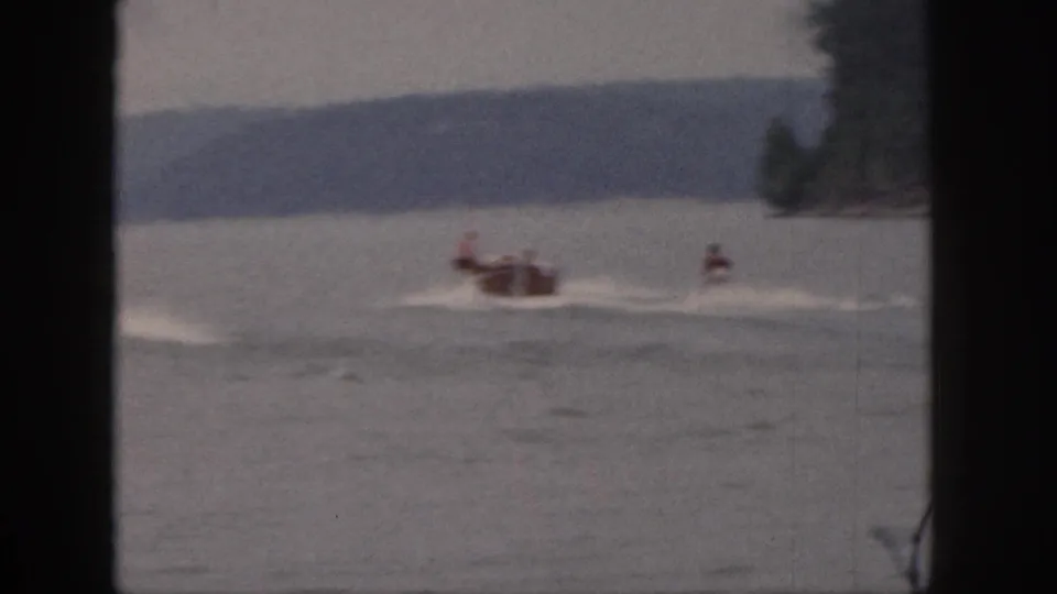 1961 Michigan home-movie frame of a small boat carrying passengers while pulling a waterskier across a lake.