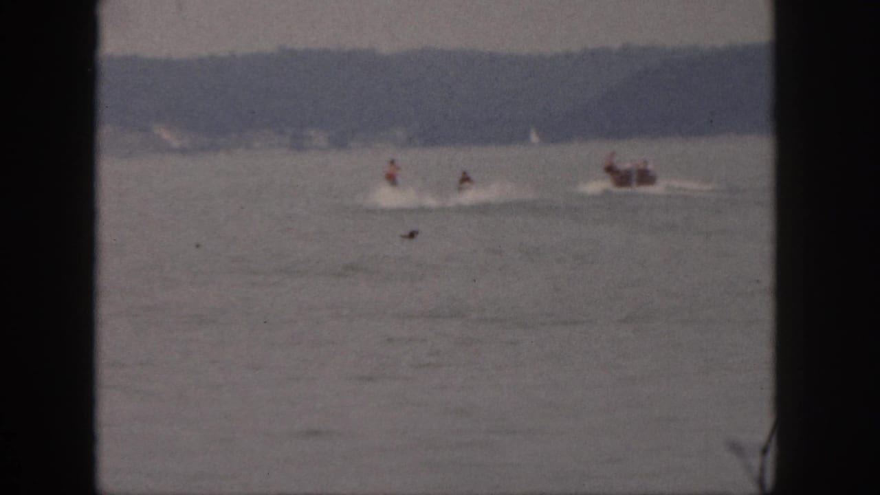 Distant watercraft riders and a small boat move along the lake near the horizon.