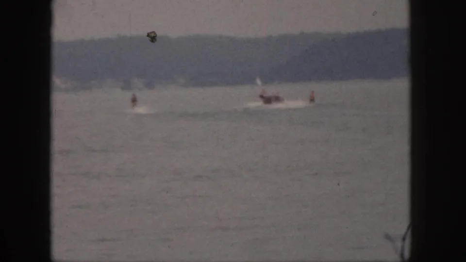 Final 1961 Michigan lake frame with a small motorboat, distant riders, low wakes, and dark 8mm frame borders.