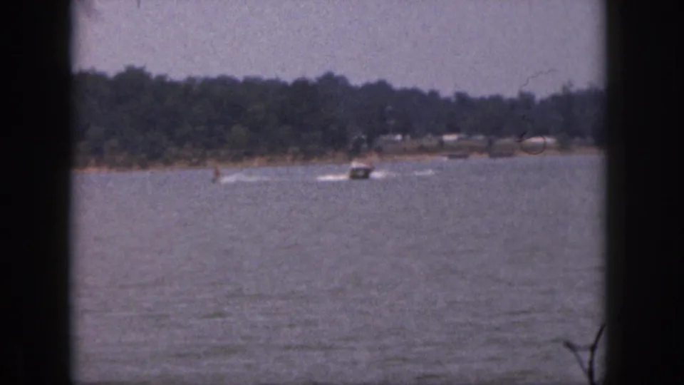 1961 Michigan 8mm frame showing a boat and water skiers passing left to right against a wooded lakeshore.