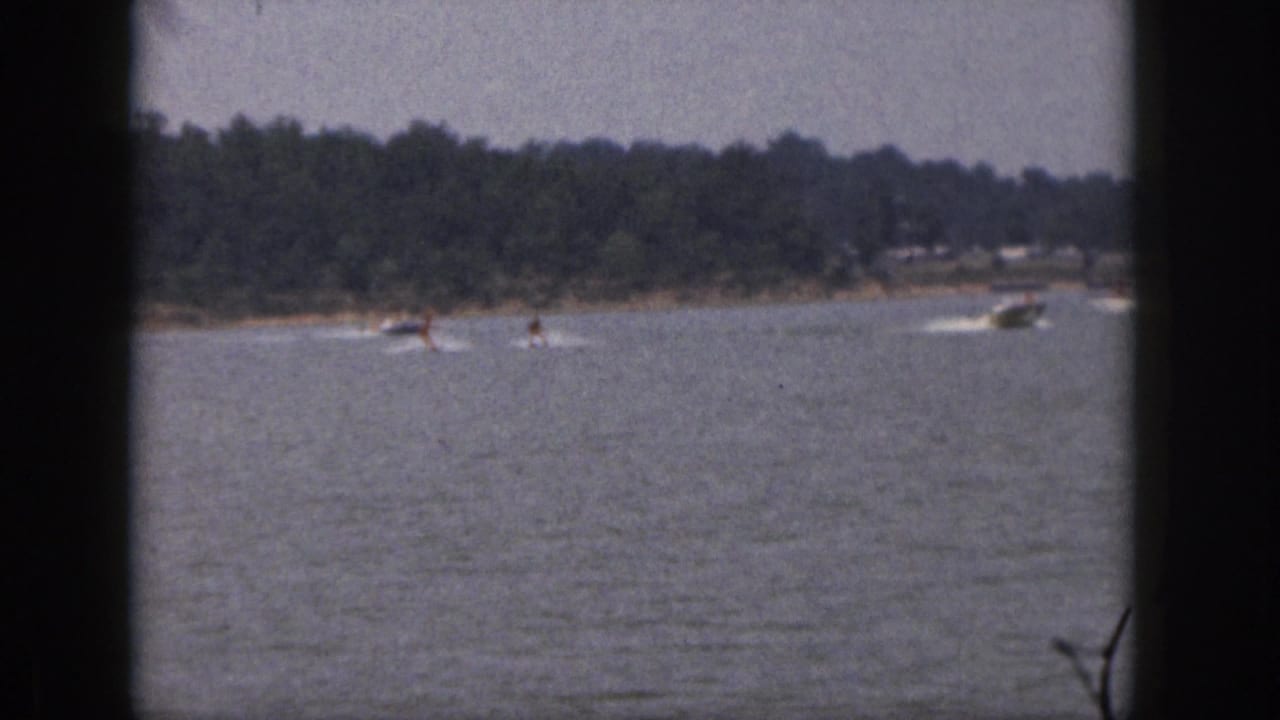 Water skiers and a motorboat travel across open water with another boat nearby.