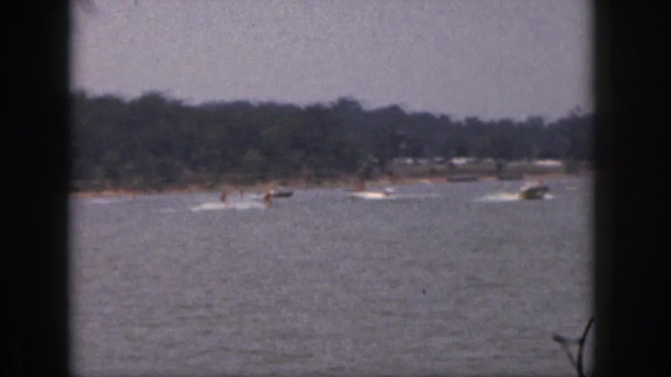 1961 Michigan lake scene with distant water skiers, a tow boat, and another motorboat crossing close by.