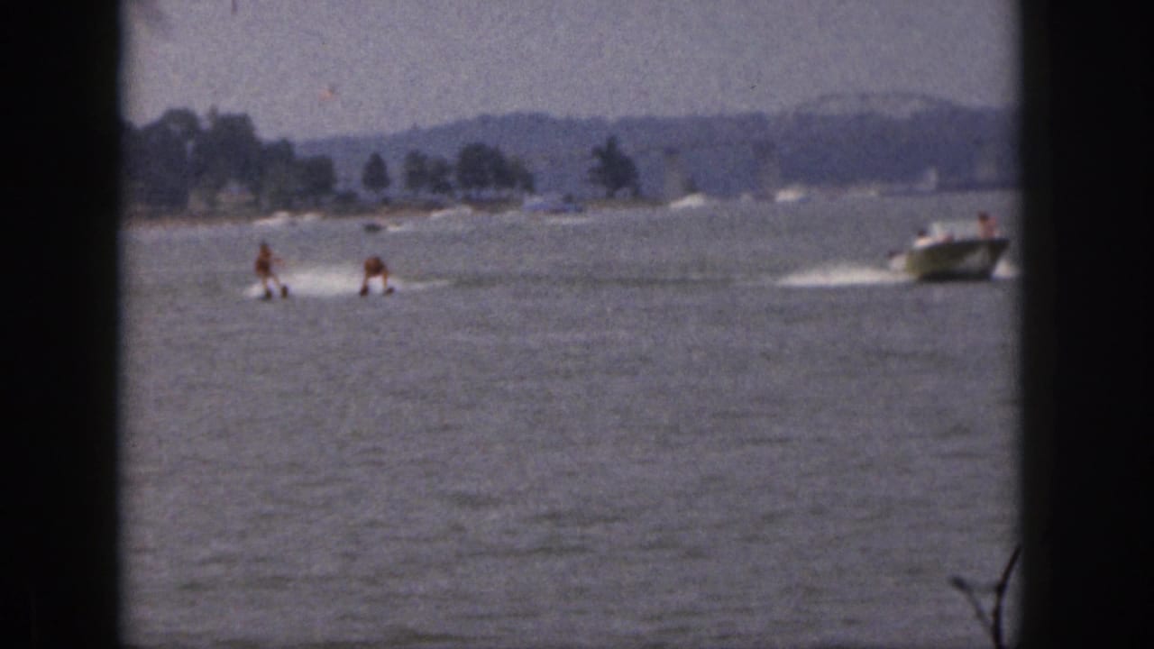 Two skiers ride across the water while a motorboat continues ahead near the right edge.