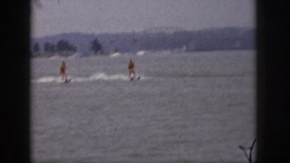 1961 Michigan 8mm frame with two skiers on open lake water, visible wakes, hazy hills, and dark film-frame edges.