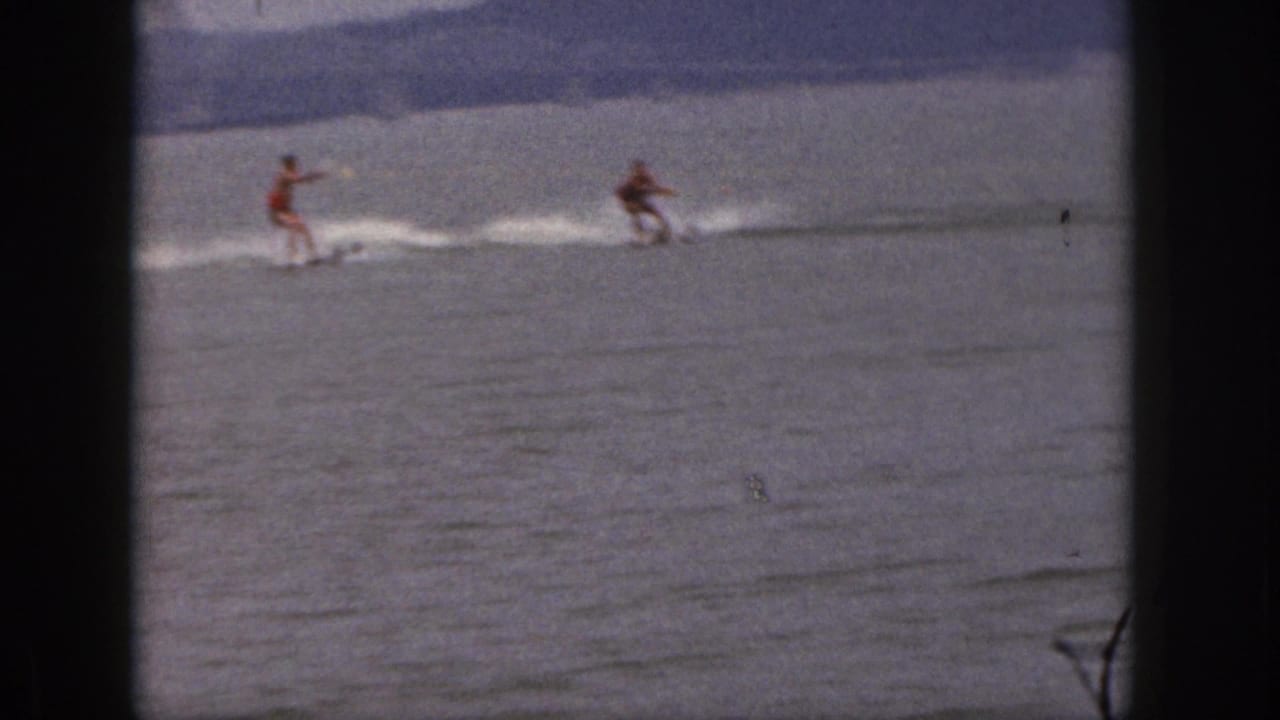 Two adult skiers are pulled across a calm Michigan lake, with soft grain and faded color from the 8mm source.