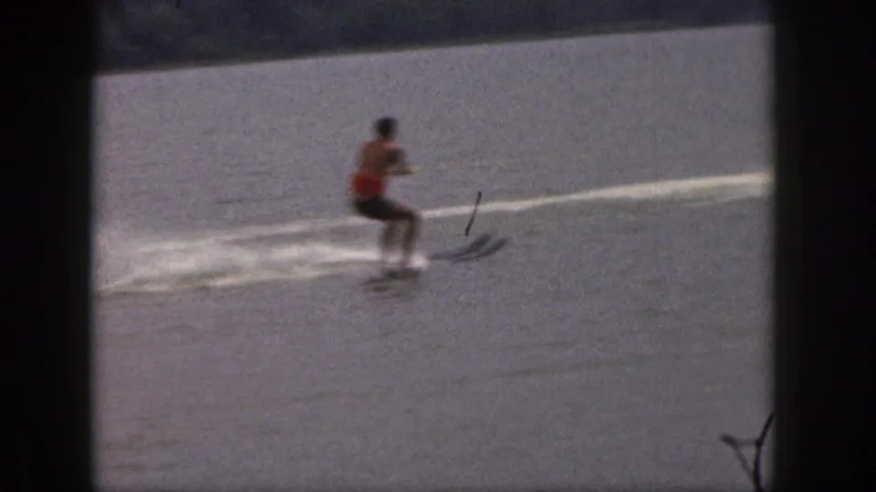 One adult water skier rides across the calm Michigan lake, framed by soft 8mm grain and faded color.