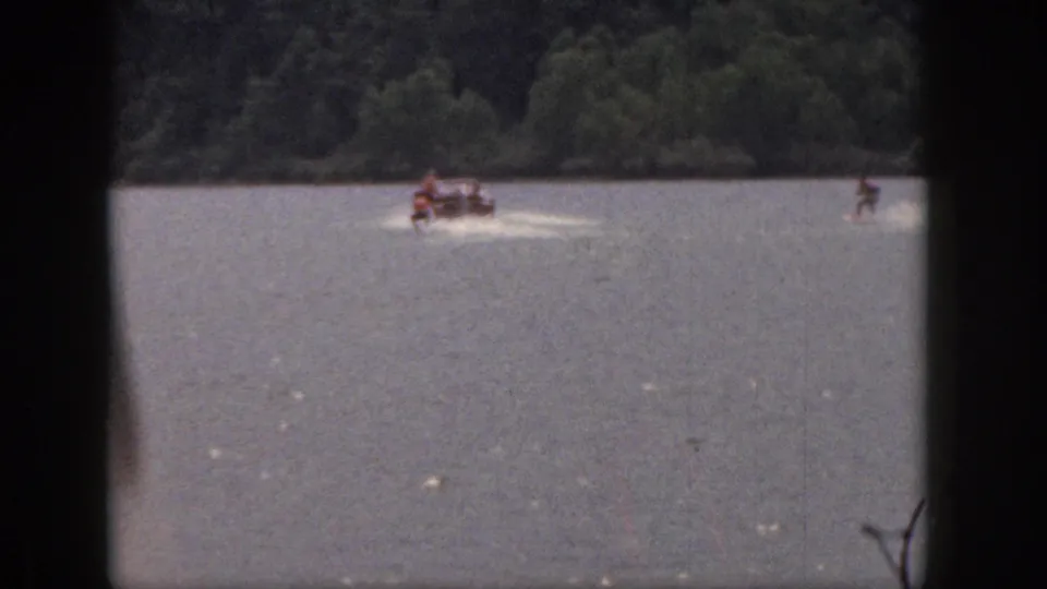Final 1961 Michigan frame with the motorboat and skiers farther away on the lake, backed by a forested shore.
