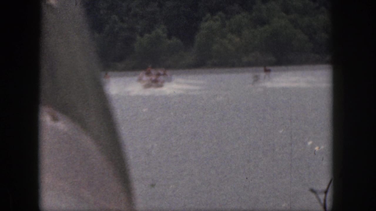 1961 Michigan 8mm home-movie view of a motorboat pulling waterskiers across a wooded lake, partly obscured by the film frame.