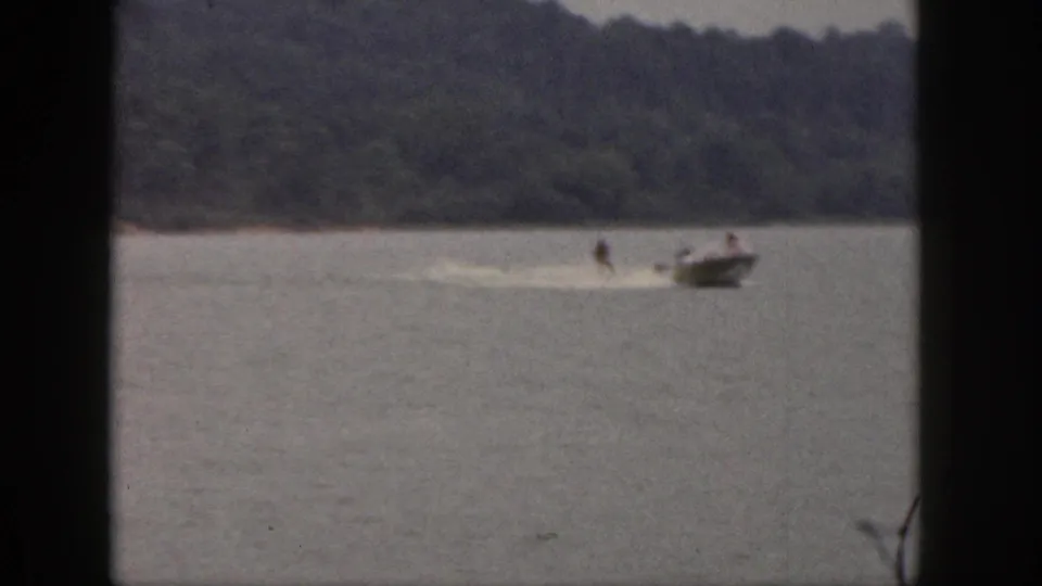 The skier remains upright behind the boat as both pass across the lake in soft 8mm color footage from Michigan.