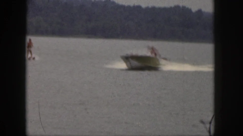 The boat appears closer in frame with the skier behind it, crossing calm lake water in 1961 Michigan home-movie footage.