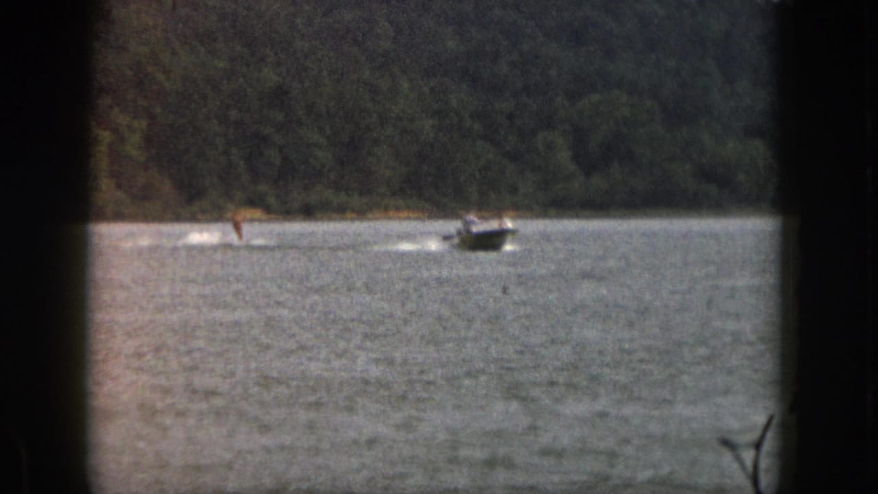 Boat and water skier continue across the lake with a forested shore behind them.