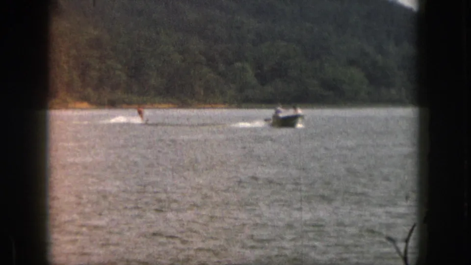 1961 Michigan home-movie frame showing a water skier behind a motorboat, seen from a distant shoreline perspective.