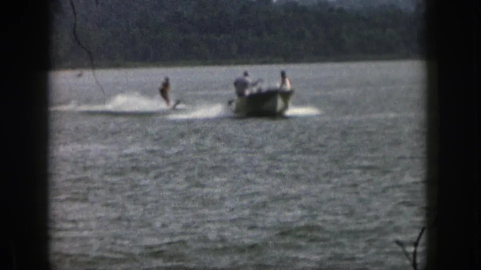 1961 Michigan waterskiing frame with a skier near the boat wake and two distant figures aboard the small motorboat.