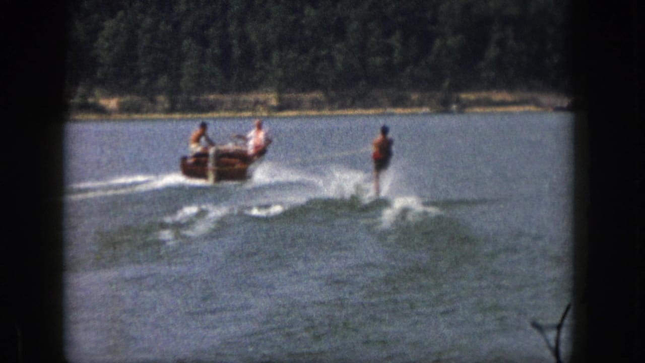 1961 Michigan 8mm frame showing a small motorboat carrying people and pulling a waterskier over a broad lake.