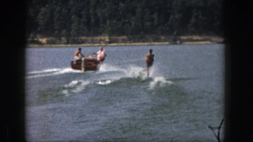 1961 Michigan 8mm frame showing a small motorboat carrying people and pulling a waterskier over a broad lake.