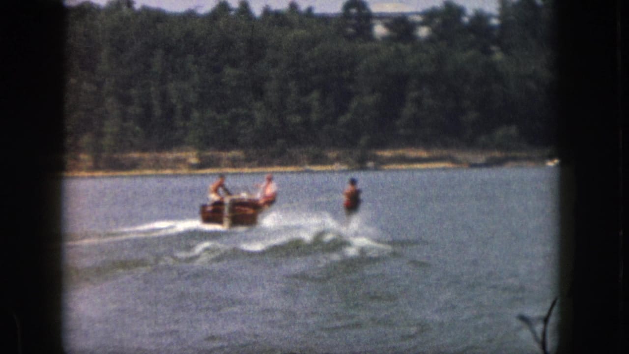 Boat and waterskier continue across open water near a tree-lined shore.