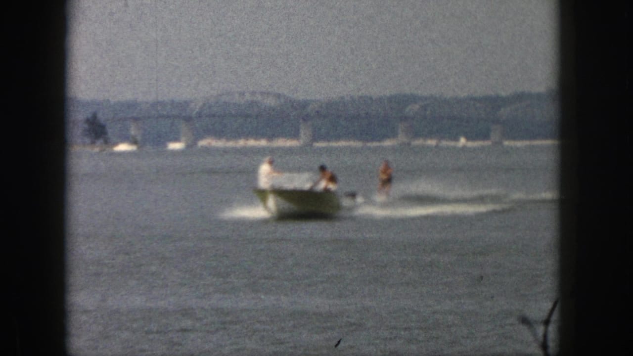 Distant Michigan lake view from 1961 showing a motorboat towing a waterskier past a far shoreline.