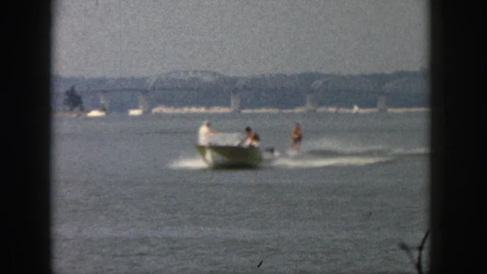 Distant Michigan lake view from 1961 showing a motorboat towing a waterskier past a far shoreline.