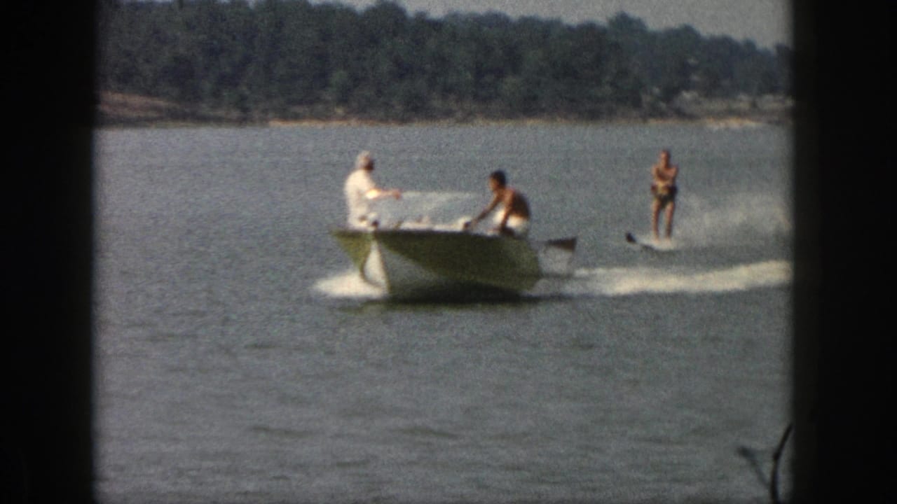 Closer 1961 Michigan home-movie view of a motorboat towing a standing water skier across the lake.