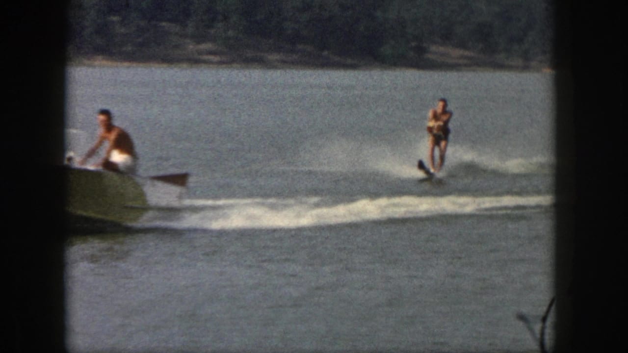 1961 Michigan home-movie frame with a partly cropped motorboat and one water skier crossing the lake wake.