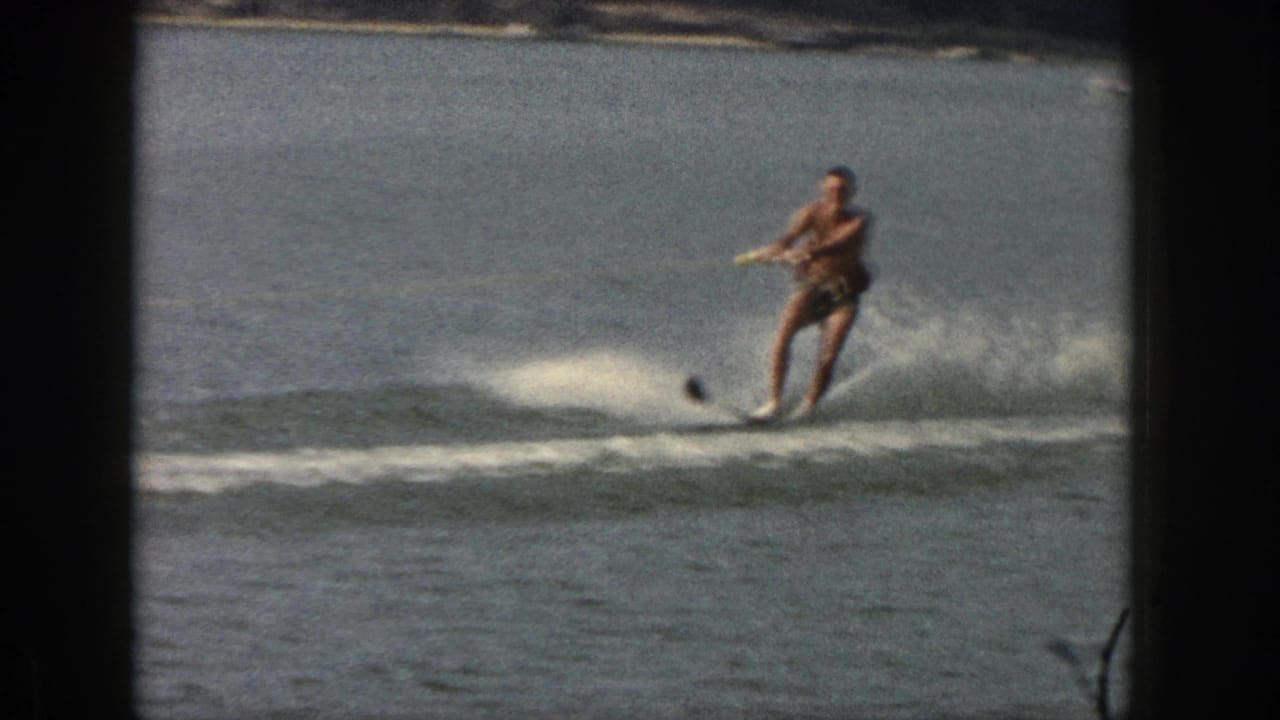 The man continues water skiing on a calm Michigan lake, holding a tow rope as the single ski cuts through the water.