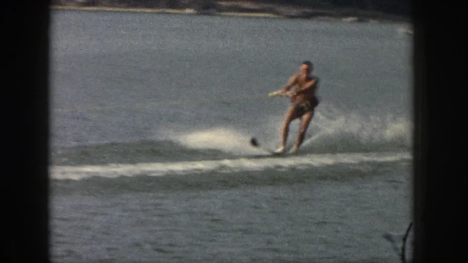 The man continues water skiing on a calm Michigan lake, holding a tow rope as the single ski cuts through the water.