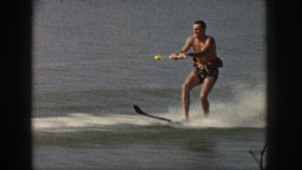 A closer 8mm frame shows the water skier in patterned trunks, knees bent and tow rope in hand, moving across the lake.