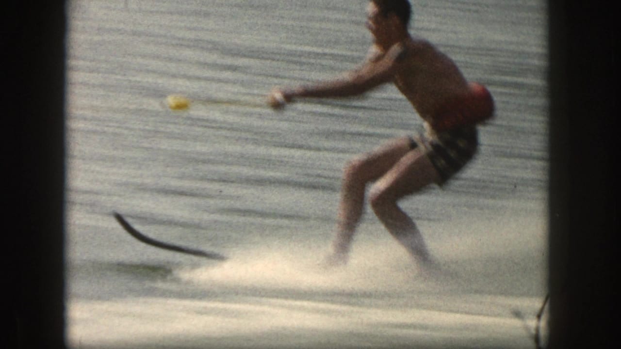 Side view of the 1961 Michigan water skier leaning into the tow rope while spray rises around the single ski.