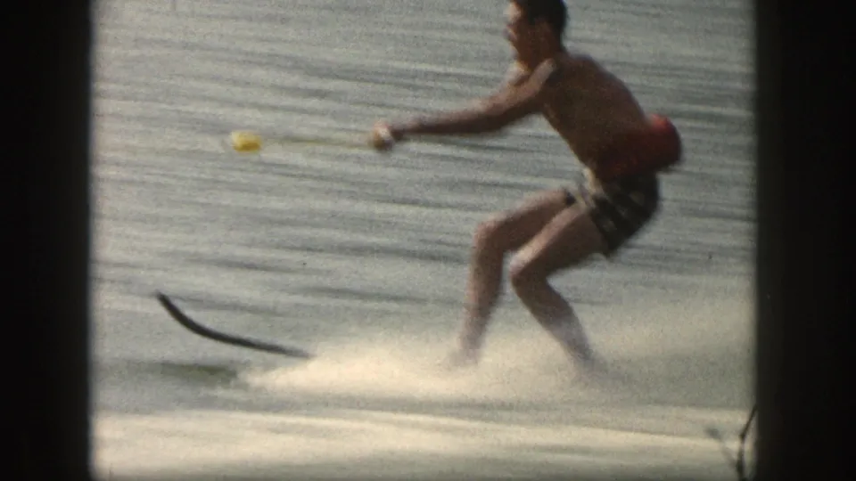 Side view of the 1961 Michigan water skier leaning into the tow rope while spray rises around the single ski.