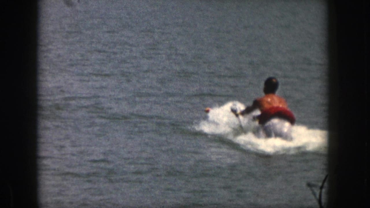 Male water skier rises behind a tow rope, making white spray on the lake.