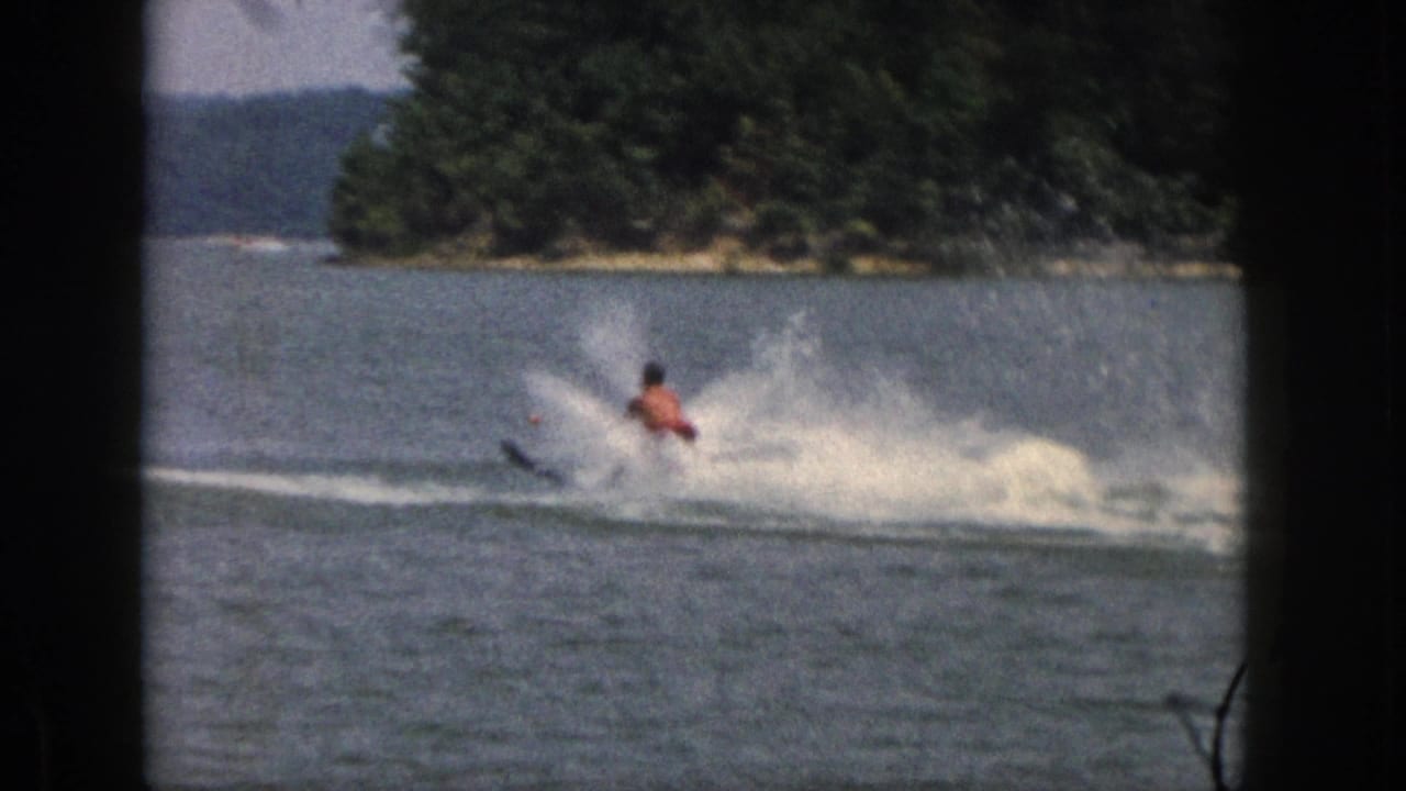 Distant water skier continues across the lake with spray trailing behind.