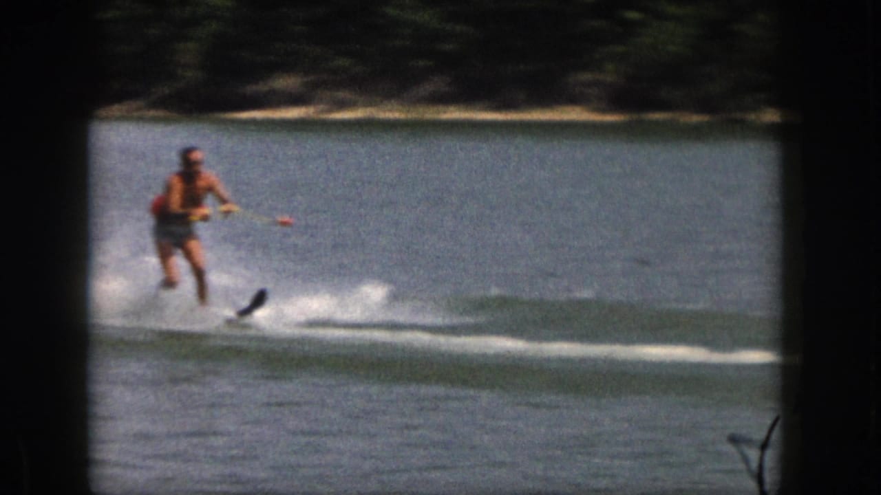 Water skier glides across the lake with a ski tip visible above the spray.