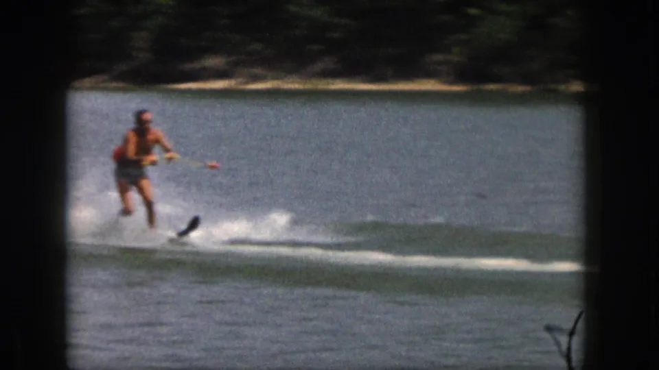 Adult man in a red life vest skis across a Michigan lake in 1961 home-movie footage.
