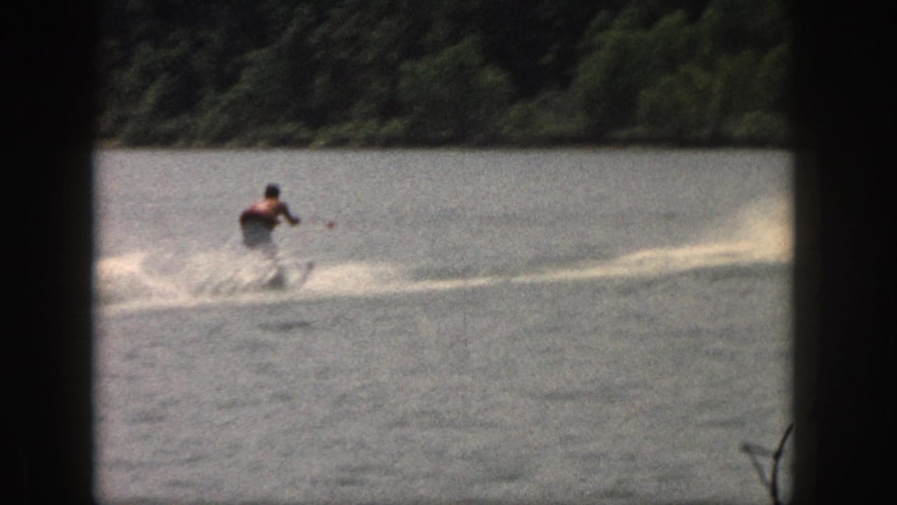Distant water skier being pulled across the lake near a wooded shoreline.
