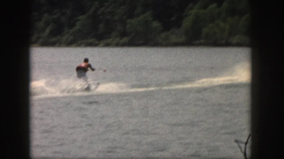Wide 1961 Michigan lake view with a water skier trailing a tow line and leaving a spray wake.