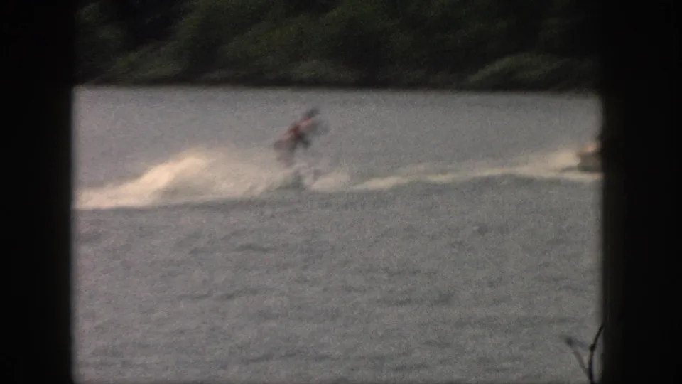 Soft 8mm frame from 1961 Michigan showing a water skier in motion with spray on a tree-lined lake.