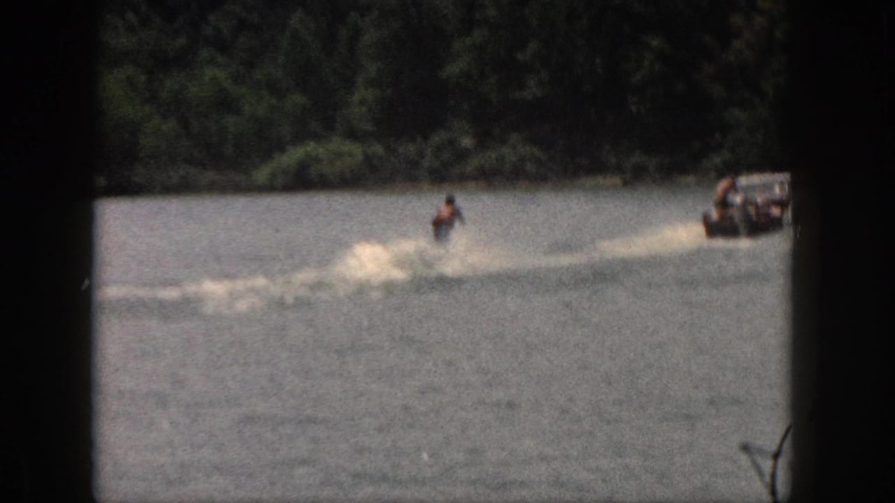 1961 Michigan 8mm frame showing a distant water skier being pulled by a motorboat across a wooded lake.