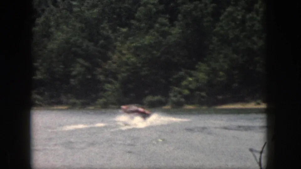 A 1961 Michigan lake frame shows the motorboat crossing near the trees with spray and wake visible.