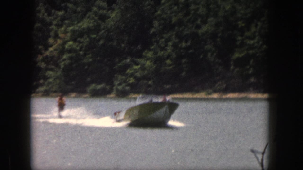 Water skier trails behind a speedboat, throwing spray across the lake.