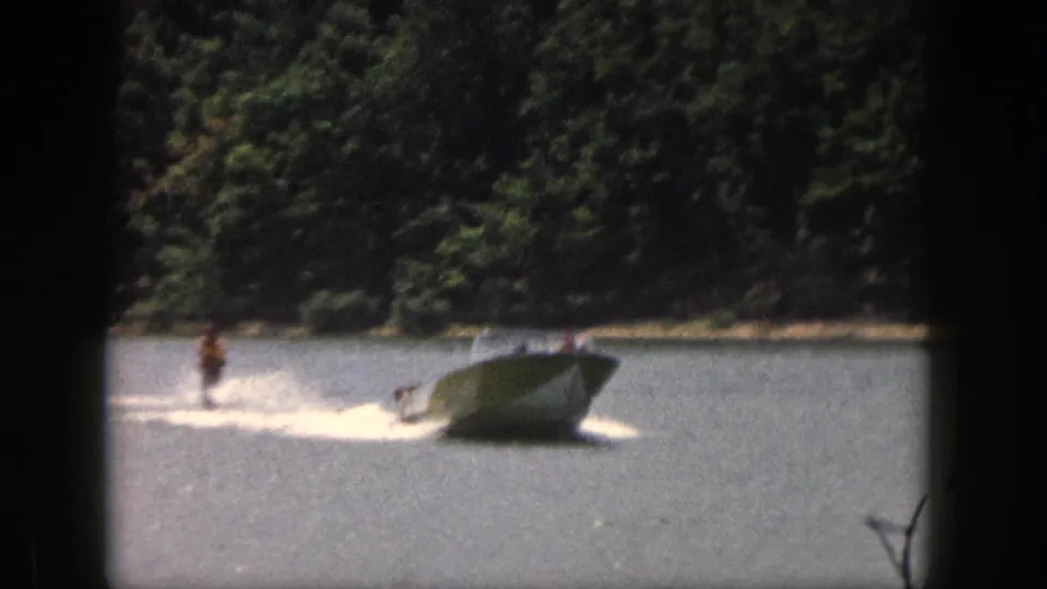 1961 Michigan home-movie frame with a man water skiing behind a speedboat on a tree-lined lake.
