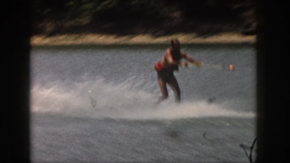 The skier passes closer to the camera on a single ski, with bright spray crossing the 1961 Michigan lake frame.
