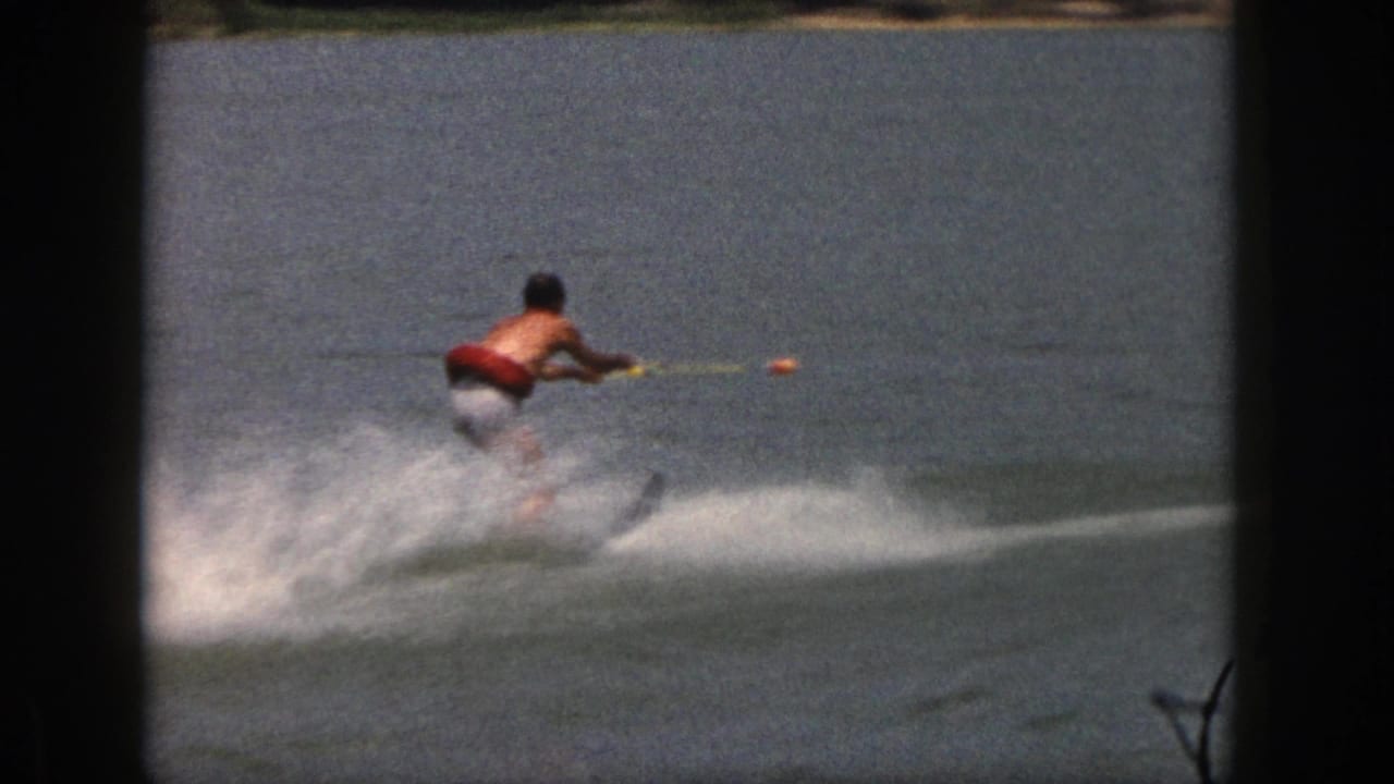 Water skier moves across open lake water with a low spray wake behind him.