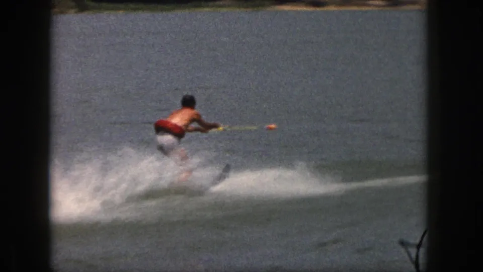 1961 Michigan lake footage shows the skier pulled by a tow rope, moving rightward across the water in soft 8mm color.