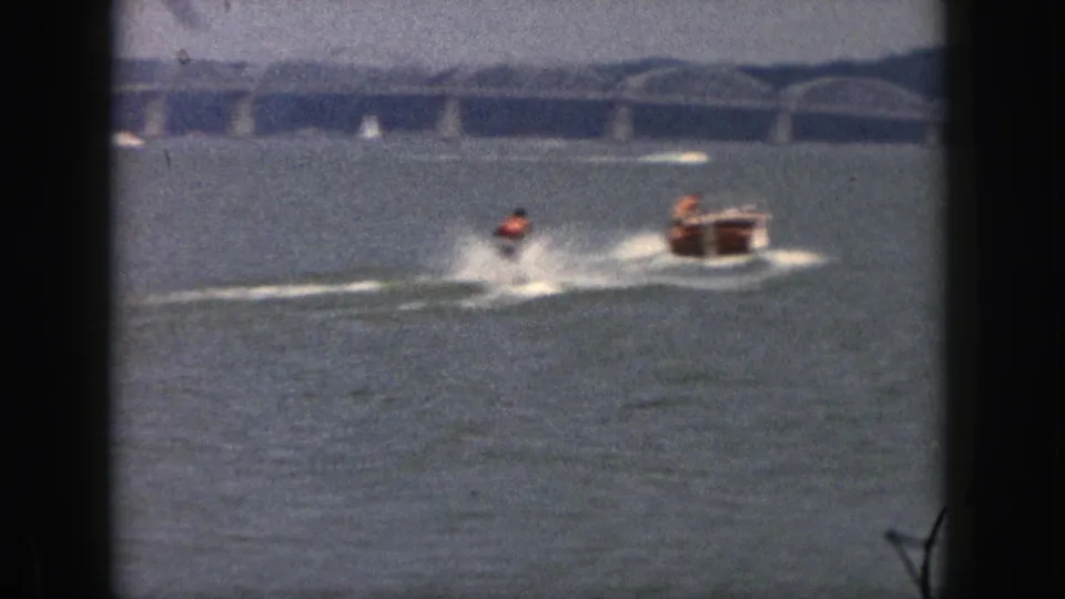 The water-skier falls into the Michigan lake in a white splash while the small tow boat continues nearby against the bridge backdrop.