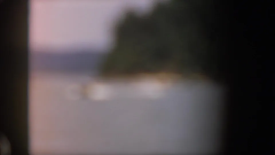 Soft, blurred 1961 Michigan lake view with a distant shoreline or tree-covered landform and dark 8mm frame edges.