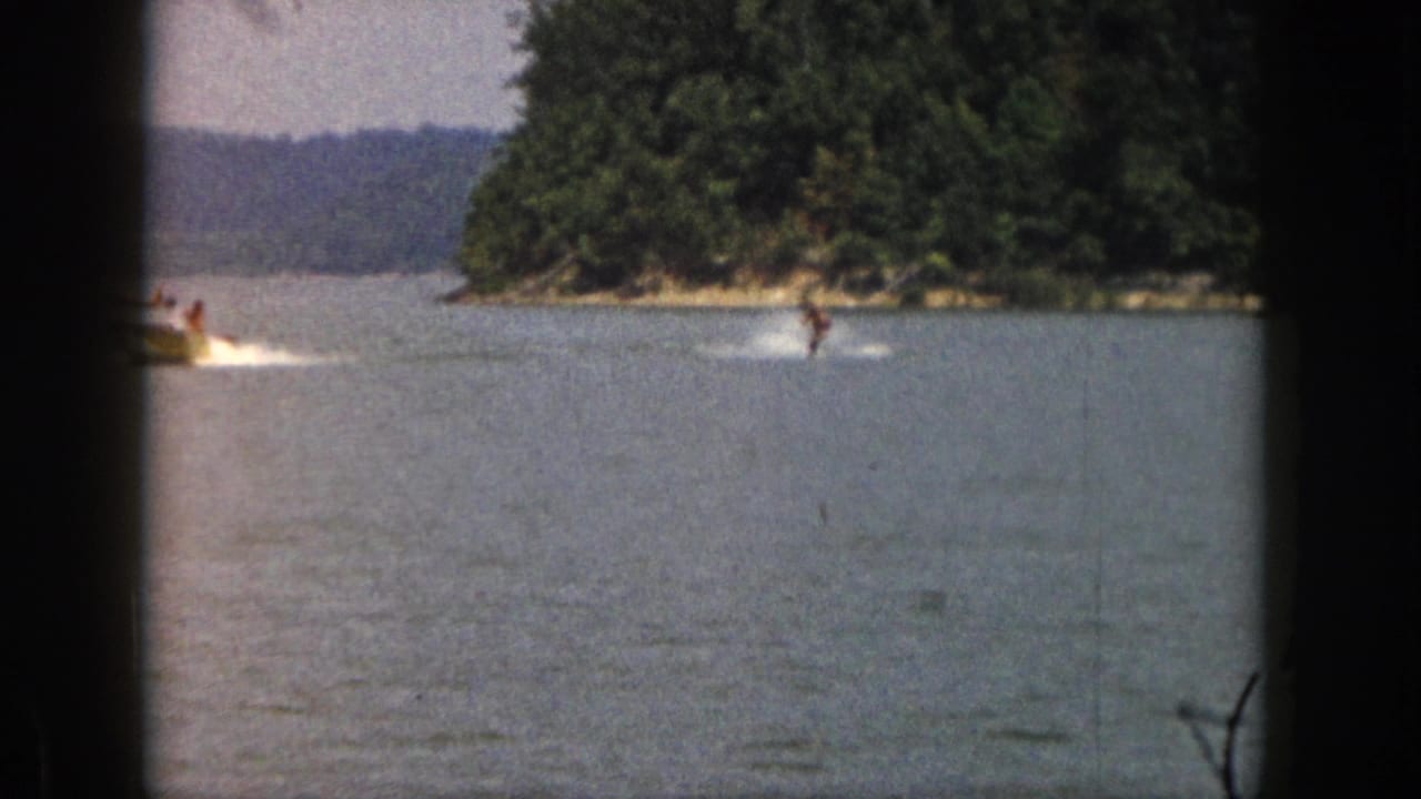Distant skier gliding behind a boat across open lake water.