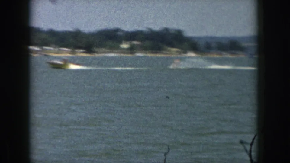 1961 Michigan home-movie frame of a boat towing a distant water-skier across open lake water.